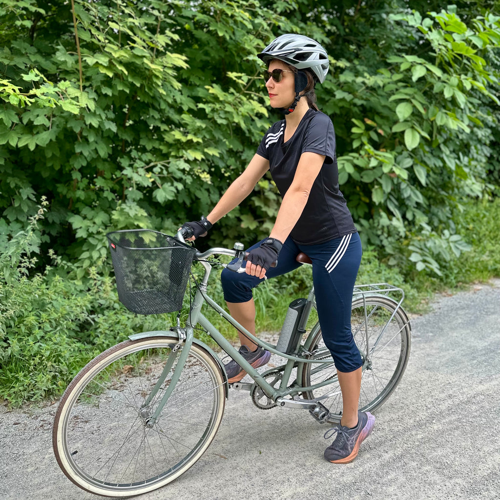 Radfahrerin mit earSHIELD Pro Windschutz am Fahrradhelm vor grünen Bäumen